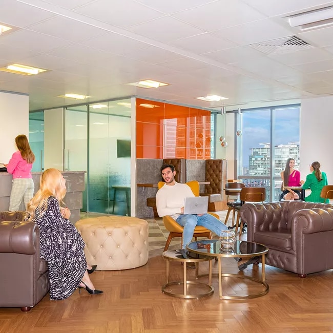 Clients working and networking at Canary Wharf coworking space with vibrant reception, and collaborative booths.