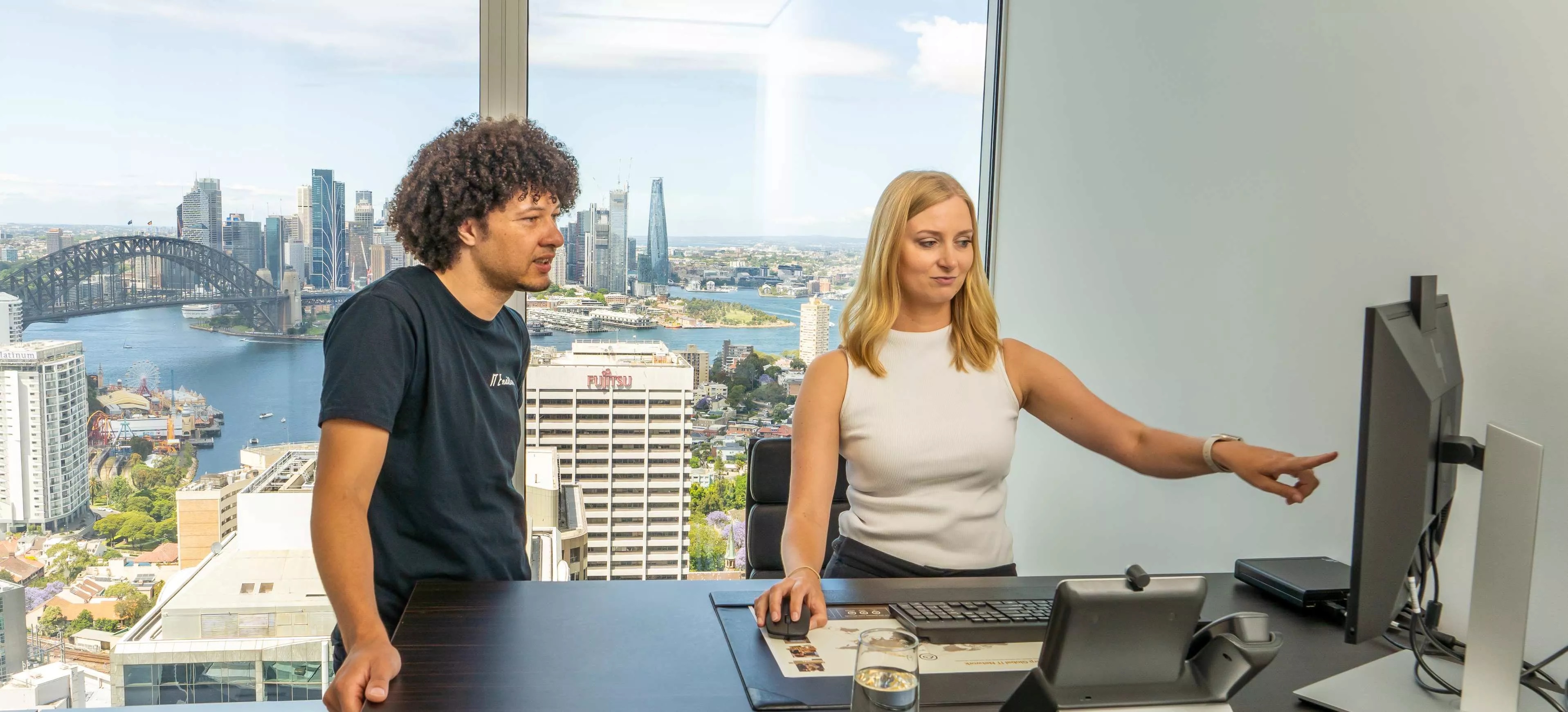 Two team members collaborating in a serviced office at Servcorp in front of city-view windows with professional tech setup.